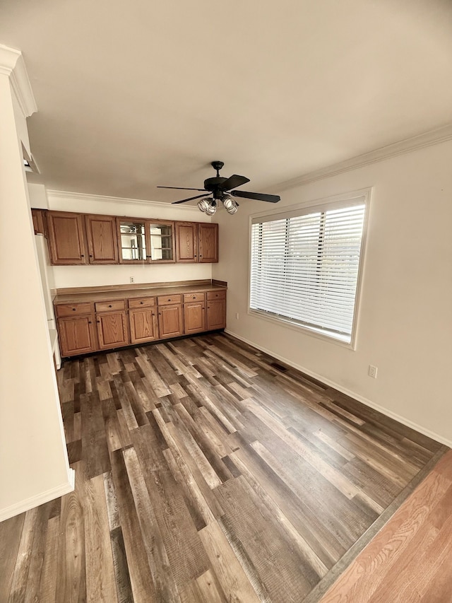 kitchen featuring brown cabinets, baseboards, crown molding, and dark wood-type flooring