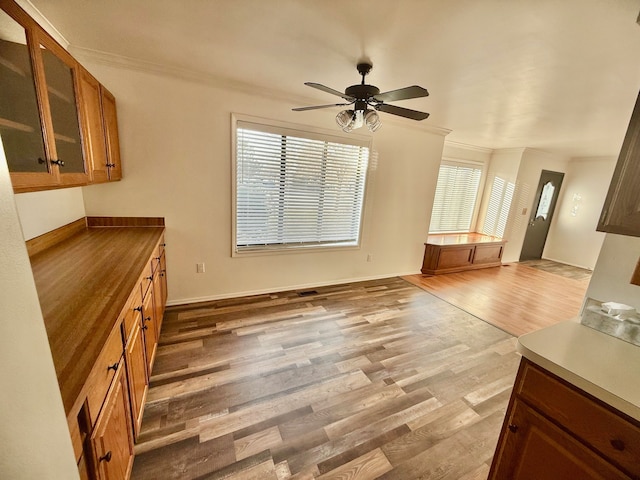 kitchen with glass insert cabinets, wood finished floors, brown cabinets, and ornamental molding