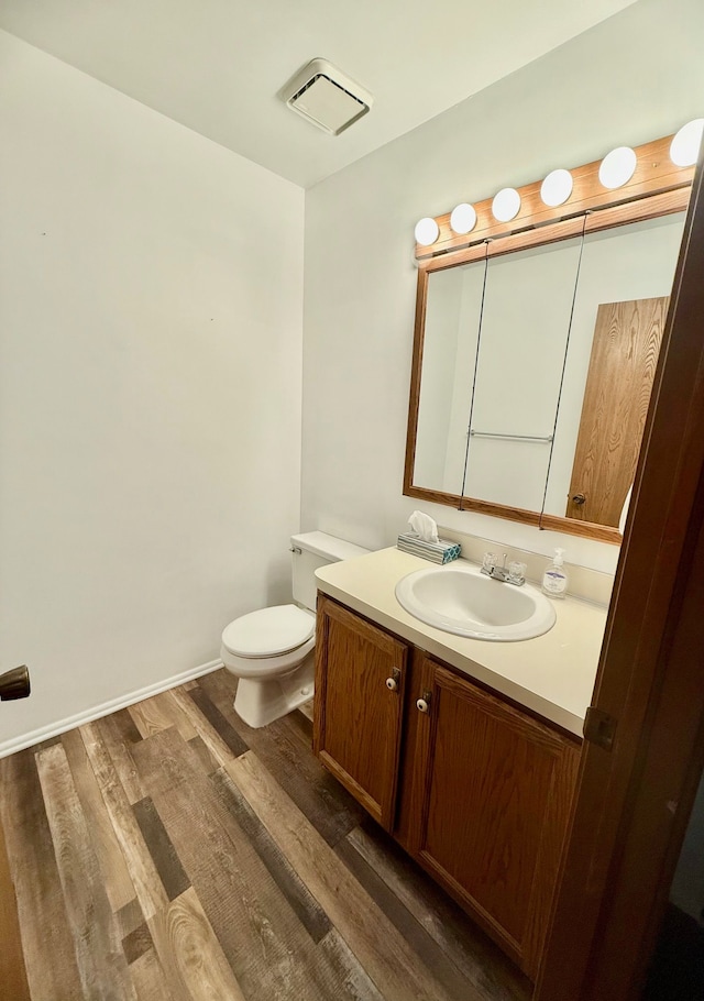 half bathroom with vanity, wood finished floors, visible vents, baseboards, and toilet