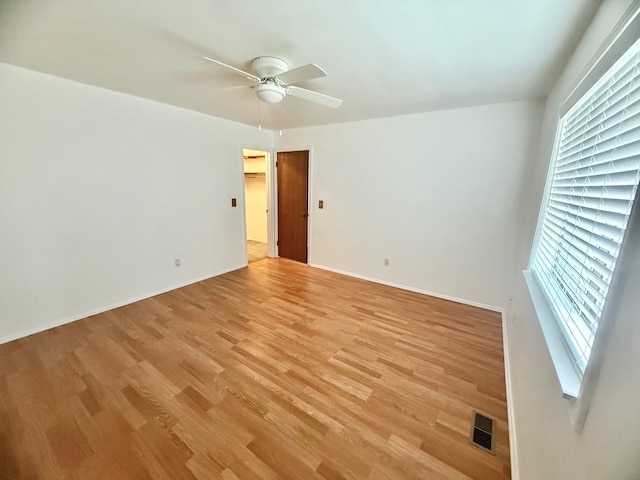 empty room featuring a ceiling fan, visible vents, light wood finished floors, and baseboards