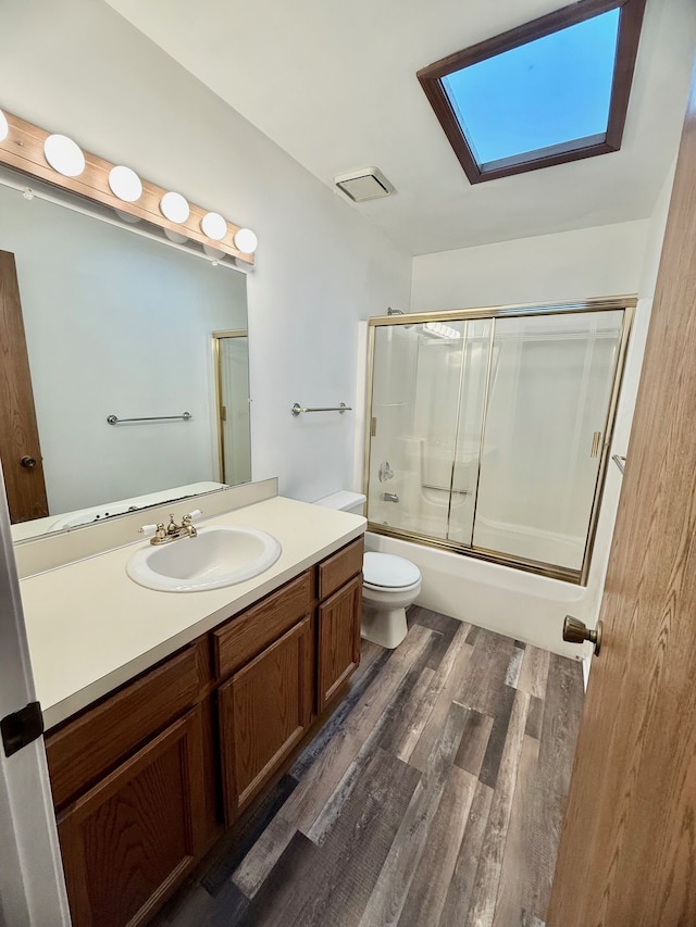 full bath with vanity, wood finished floors, enclosed tub / shower combo, a skylight, and toilet