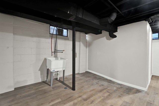 basement featuring wood finished floors, baseboards, and a sink