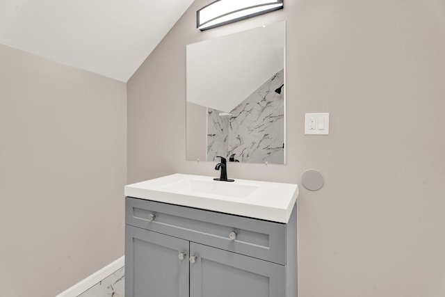 bathroom featuring baseboards, marble finish floor, vanity, and vaulted ceiling