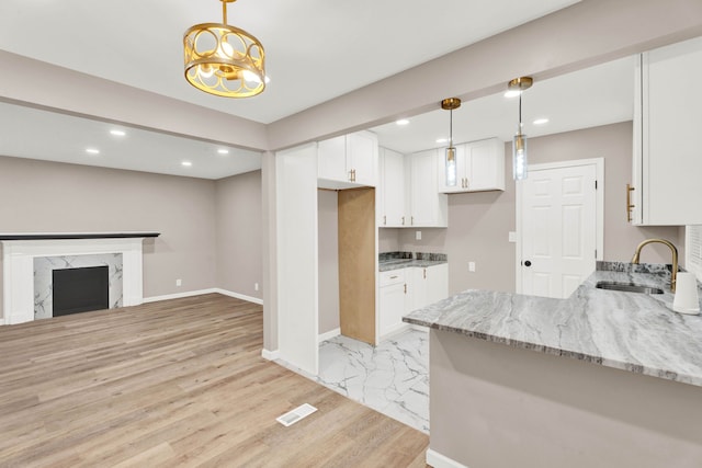 kitchen featuring a sink, light stone countertops, a fireplace, and white cabinetry