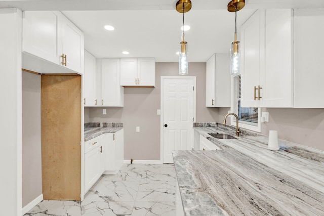 kitchen with marble finish floor, a sink, light stone counters, white cabinetry, and baseboards