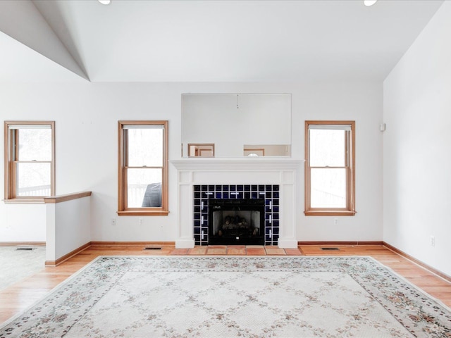 unfurnished living room featuring baseboards, wood finished floors, a tile fireplace, and vaulted ceiling