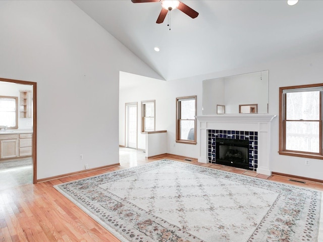 unfurnished living room featuring a tiled fireplace, light wood-style flooring, and a healthy amount of sunlight