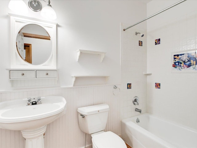 bathroom featuring a wainscoted wall, toilet, shower / bathing tub combination, and a sink