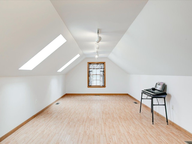 additional living space with visible vents, vaulted ceiling with skylight, wood finished floors, and baseboards