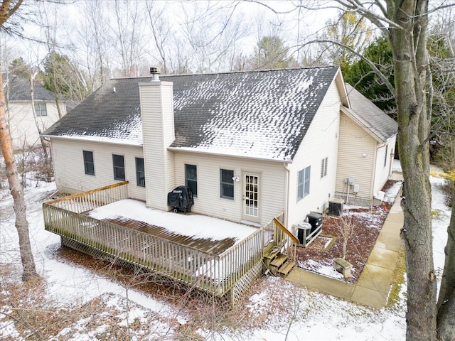 snow covered house featuring a deck, a shingled roof, and a chimney