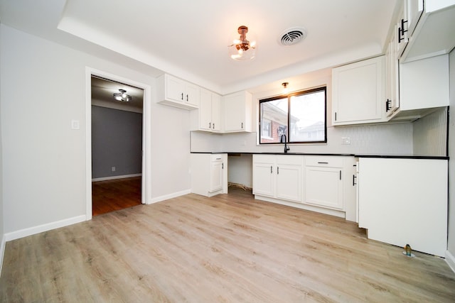 kitchen with visible vents, light wood-style flooring, dark countertops, built in desk, and white cabinets