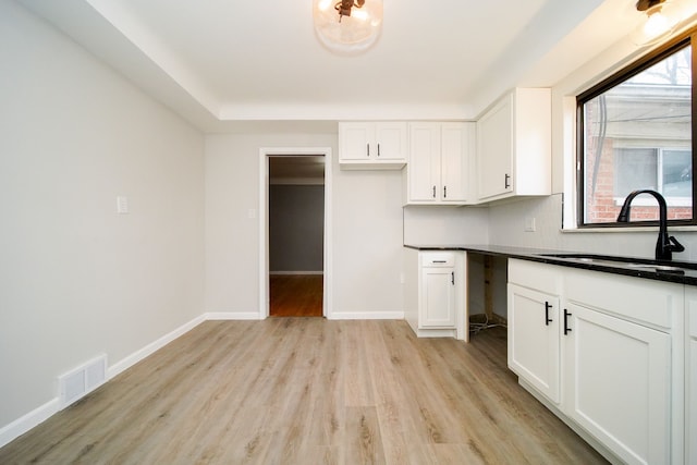 kitchen with visible vents, light wood-type flooring, a sink, dark countertops, and baseboards