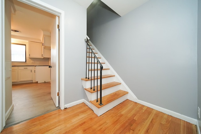 staircase with visible vents, wood finished floors, and baseboards