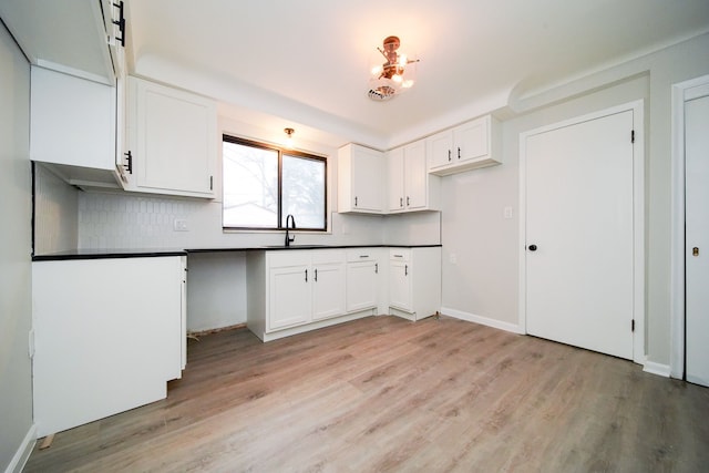 kitchen with dark countertops, decorative backsplash, light wood-style flooring, and a sink