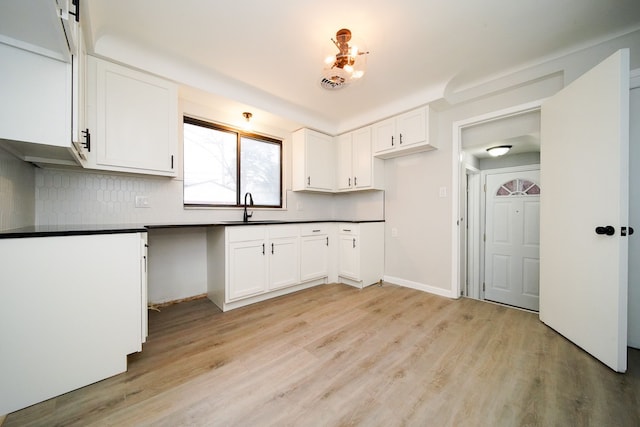 kitchen featuring a sink, light wood-style floors, white cabinetry, dark countertops, and tasteful backsplash