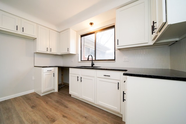 kitchen featuring dark countertops, white cabinets, light wood-style flooring, and a sink