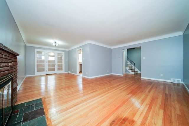 unfurnished living room featuring visible vents, wood finished floors, a glass covered fireplace, stairway, and baseboards