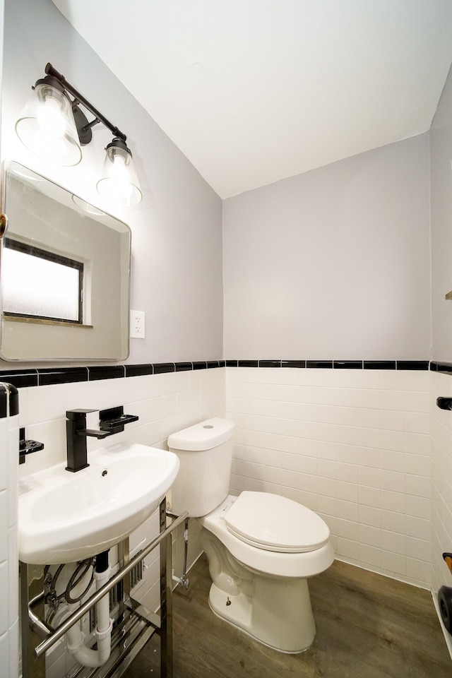 half bathroom with toilet, wood finished floors, a wainscoted wall, and a sink