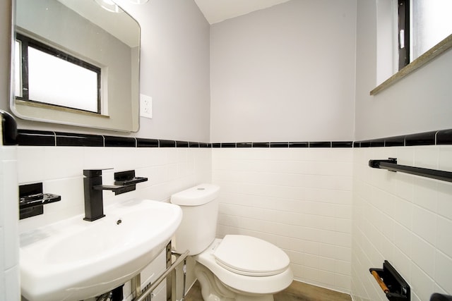 half bath with wainscoting, toilet, tile walls, and a sink