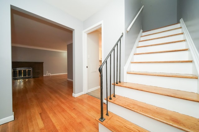 stairway with baseboards, a brick fireplace, and wood finished floors