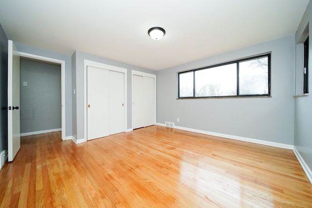 unfurnished bedroom with light wood-style flooring, baseboards, visible vents, and two closets