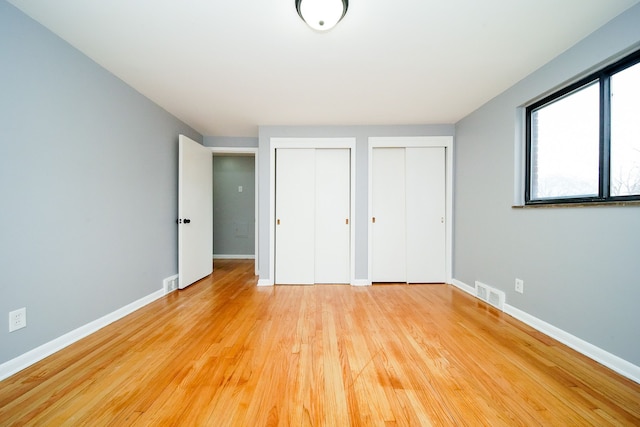 unfurnished bedroom featuring light wood-style floors, visible vents, baseboards, and two closets