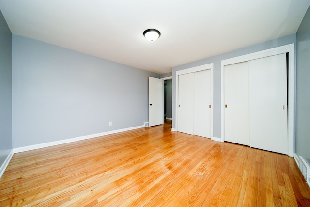 unfurnished bedroom featuring baseboards, two closets, and light wood-style flooring