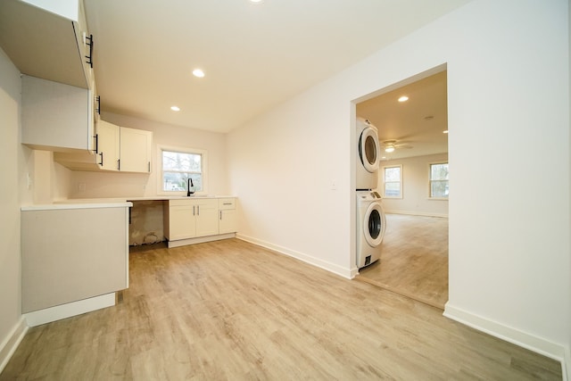 laundry area featuring baseboards, light wood-type flooring, recessed lighting, stacked washer and clothes dryer, and a sink