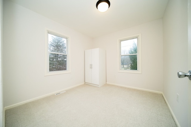 unfurnished room with visible vents, light colored carpet, baseboards, and a wealth of natural light