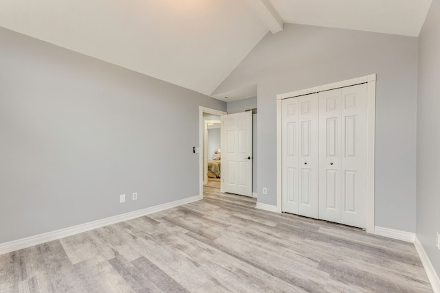 unfurnished bedroom featuring lofted ceiling with beams, baseboards, light wood-type flooring, and a closet