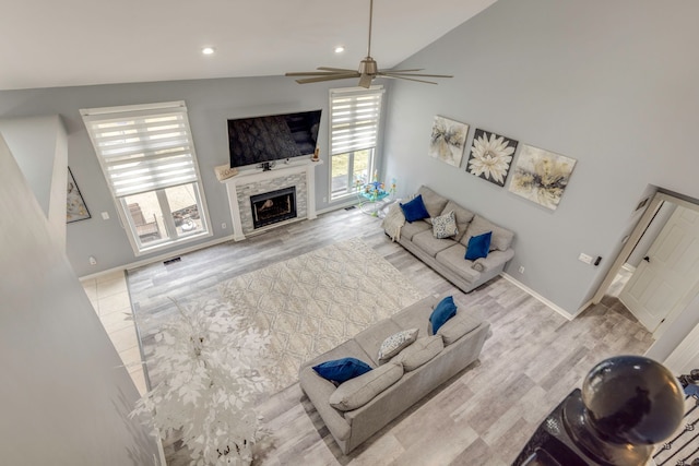 living area featuring a tiled fireplace, lofted ceiling, baseboards, and visible vents