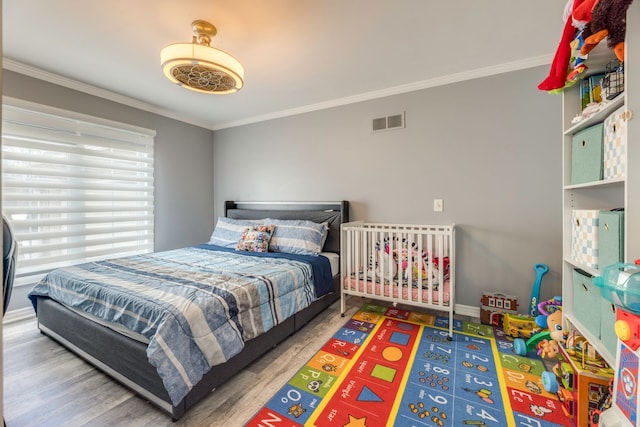 bedroom featuring visible vents, baseboards, wood finished floors, and crown molding