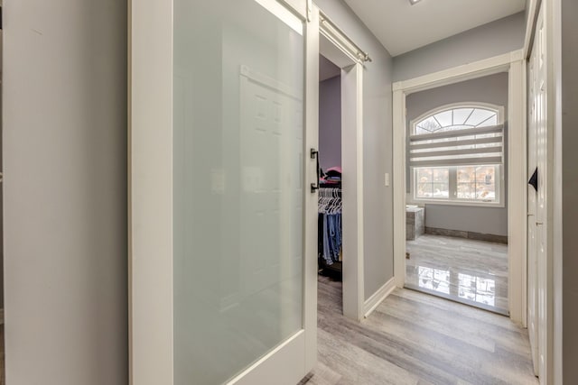 hall featuring light wood-type flooring, a barn door, and baseboards