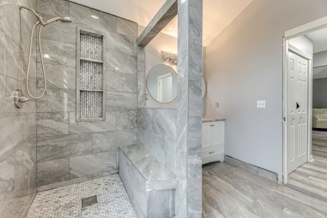 bathroom featuring tiled shower, vanity, baseboards, and wood finished floors