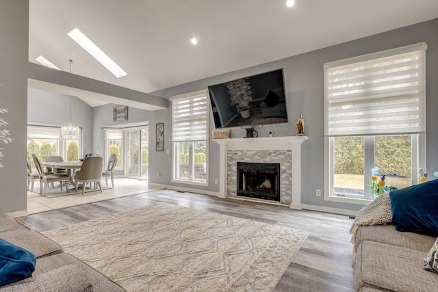 living room with baseboards, a fireplace, a skylight, wood finished floors, and high vaulted ceiling