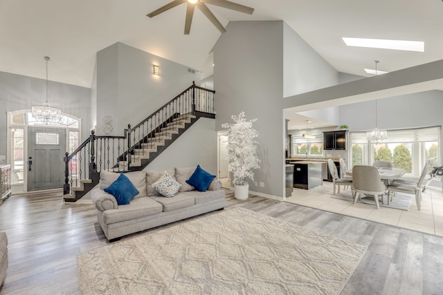 living room with high vaulted ceiling, ceiling fan with notable chandelier, light wood-type flooring, and stairs