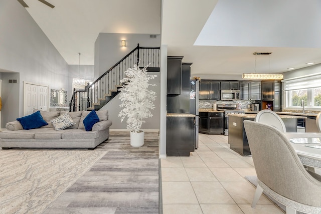 living area featuring visible vents, stairway, light tile patterned floors, an inviting chandelier, and high vaulted ceiling