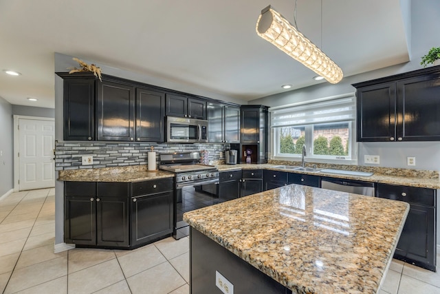 kitchen with light stone counters, a sink, stainless steel appliances, dark cabinets, and backsplash