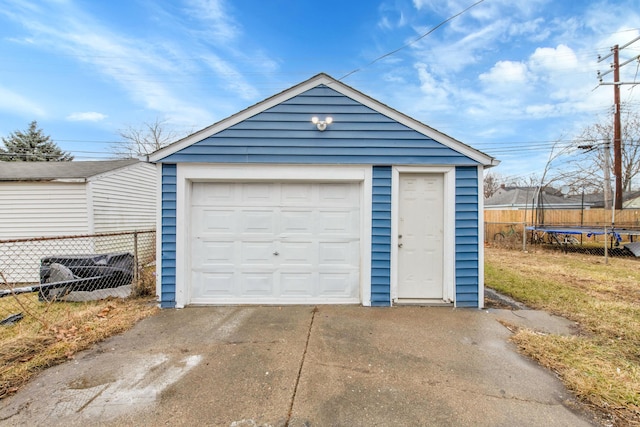 detached garage featuring a trampoline, driveway, and fence