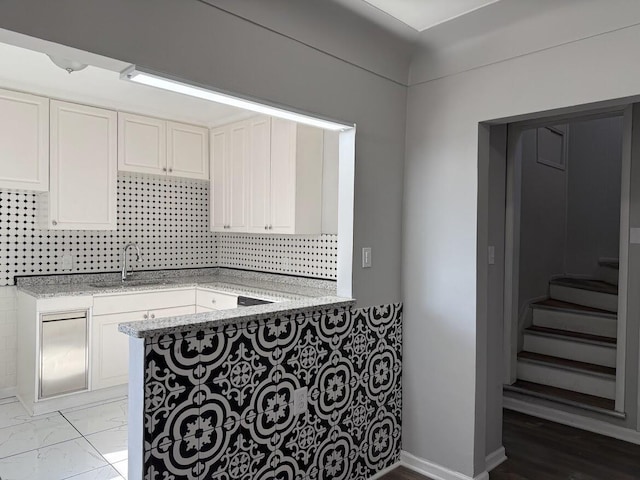 kitchen with light stone counters, decorative backsplash, white cabinetry, and a sink