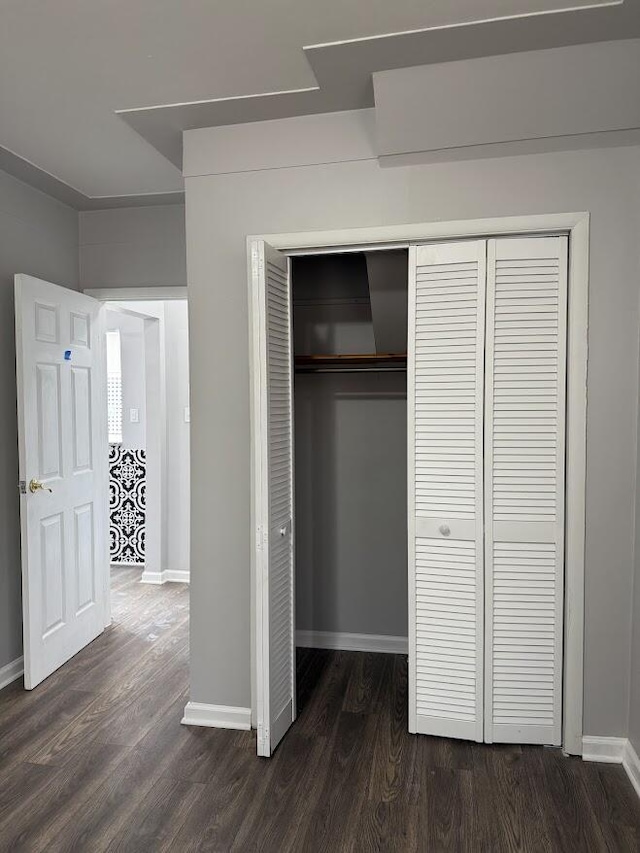 unfurnished bedroom with a closet, dark wood finished floors, and baseboards