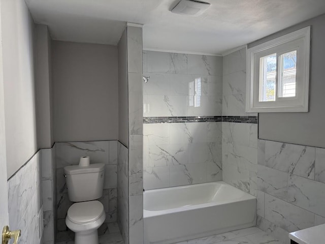 bathroom with toilet, shower / tub combination, wainscoting, marble finish floor, and tile walls