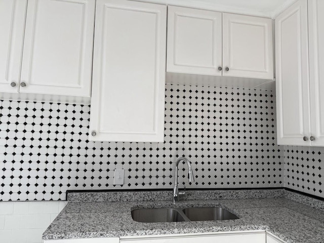 kitchen with white cabinetry, light stone counters, and a sink