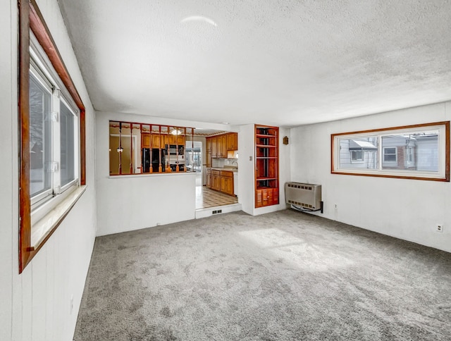 unfurnished living room featuring heating unit, a textured ceiling, and light carpet