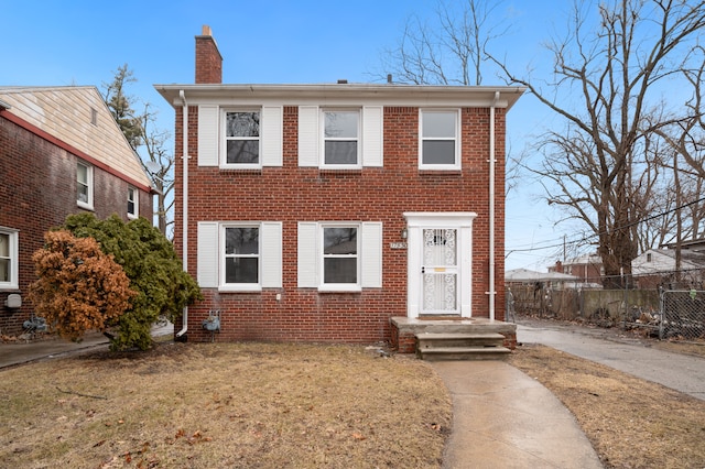 view of front of house with brick siding, a chimney, a front yard, and fence