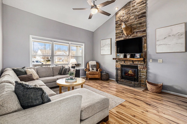 living room with wood finished floors, baseboards, high vaulted ceiling, ceiling fan, and a stone fireplace