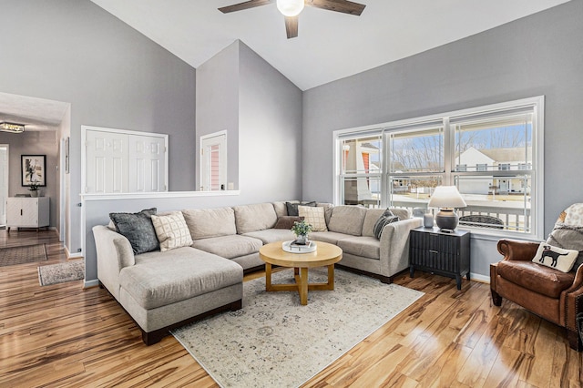 living area with baseboards, wood-type flooring, high vaulted ceiling, and a ceiling fan