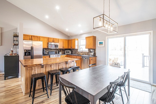 kitchen featuring a center island, vaulted ceiling, appliances with stainless steel finishes, wood counters, and a sink