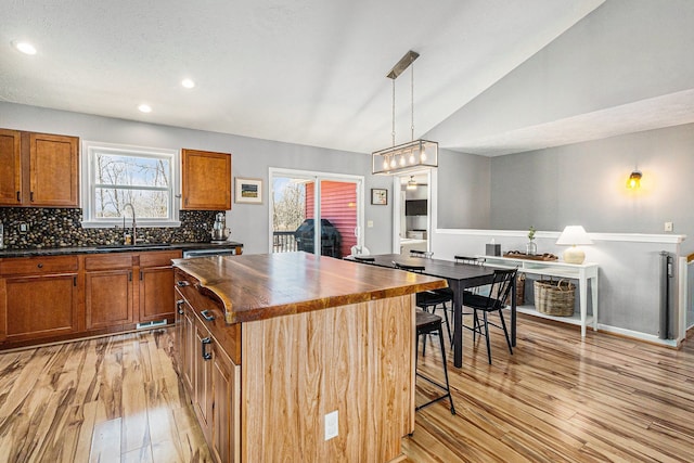 kitchen featuring light wood-type flooring, a breakfast bar, a sink, vaulted ceiling, and tasteful backsplash