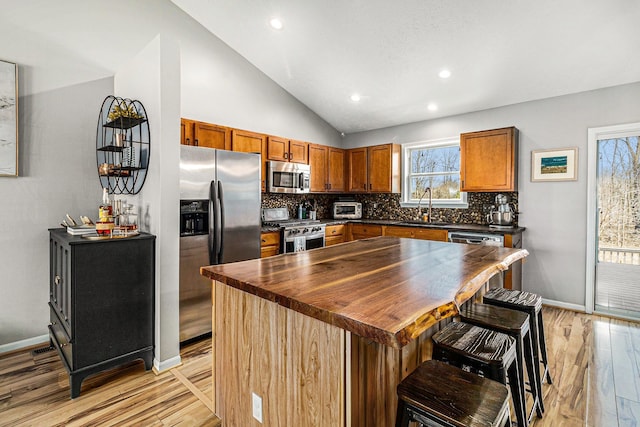 kitchen with a sink, stainless steel appliances, vaulted ceiling, wood counters, and tasteful backsplash